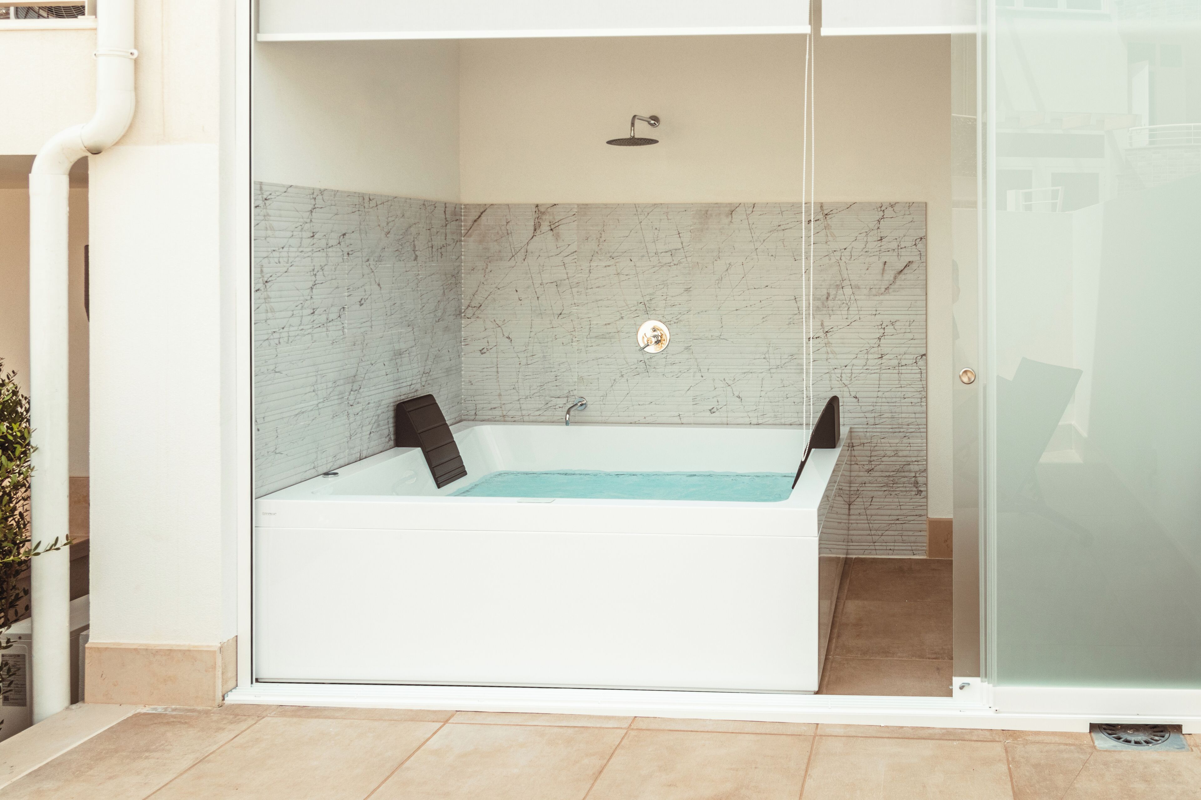 Un baño moderno con una bañera de hidromasaje con mampara de vidrio, paredes de mármol y ducha a la vista.
