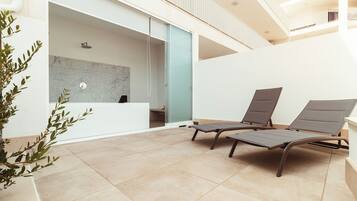 Un espacio interior moderno con una recepción, dos sillones y piso de baldosas.