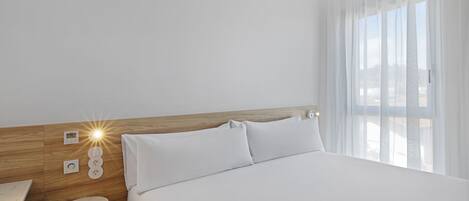 Ett modernt hotellrum med en stor säng, ett träfärgat sänggavel, ett nattduksbord och ett litet runt bord.