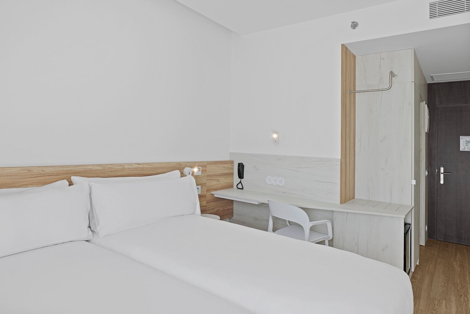 Habitación de hotel con una cama grande, un escritorio con silla, un teléfono y una puerta.