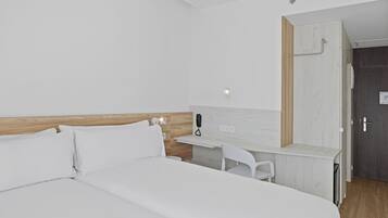 A hotel room with a large bed, a desk with a chair, a phone, and a door.