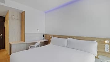 A modern hotel room with a large bed, a wooden headboard, a desk with a chair, and a built-in vanity with a mirror.