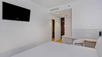 Une chambre d’hôtel moderne, dotée d’un grand lit, d’un bureau avec une chaise, d’un téléviseur fixé au mur et d’une porte en bois.