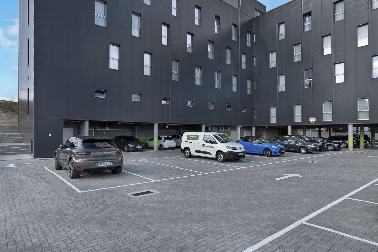 A modern building with multiple parking spaces and a white van parked in front.