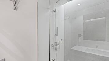 Un baño moderno con ducha de mampara de vidrio, lavamanos integrado y espejo.