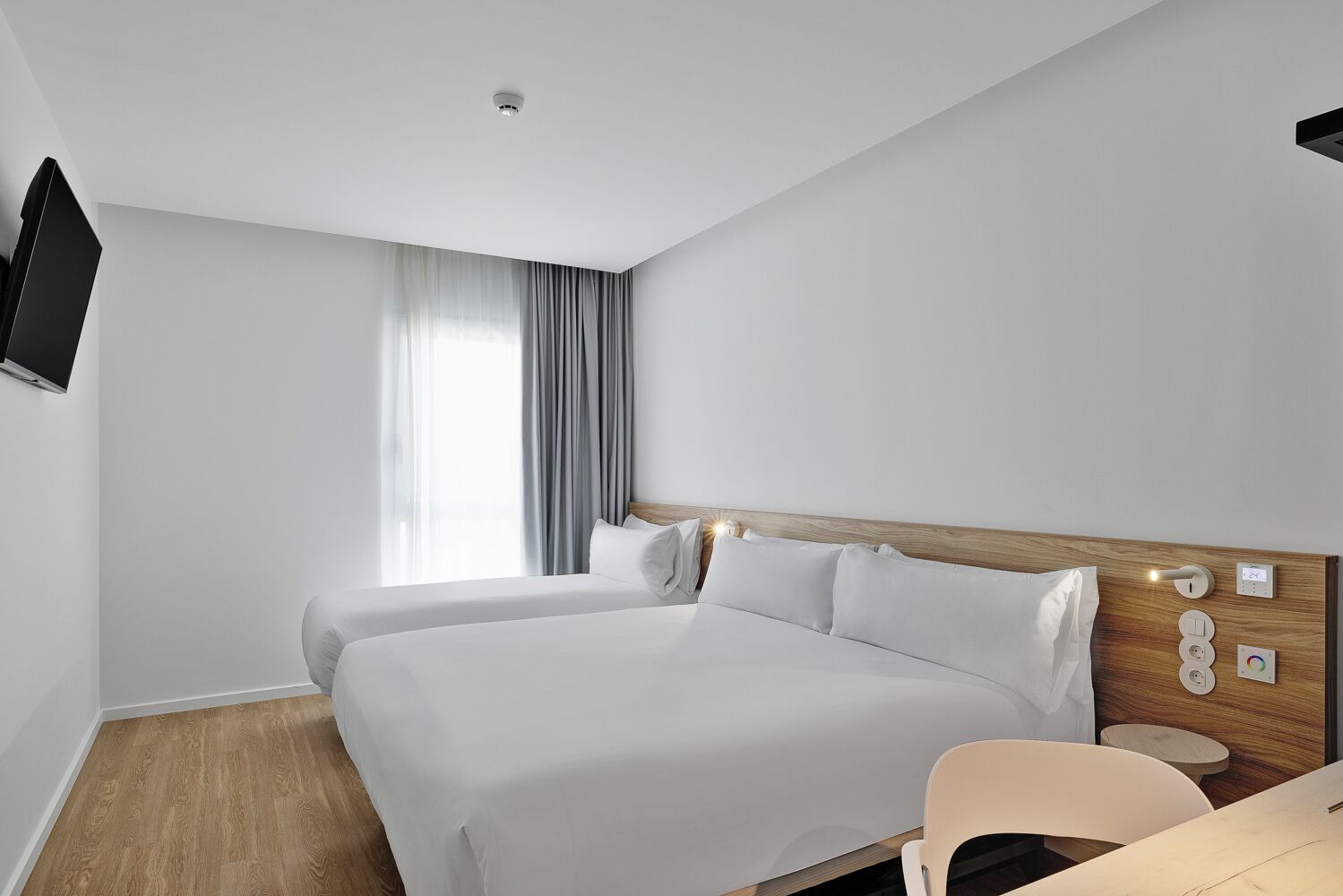 Ein modernes Hotelzimmer mit zwei Betten, einem Schreibtisch und einem an der Wand befestigten Fernseher.