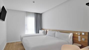 Quarto de hotel moderno com duas camas, uma escrivaninha e uma TV fixada na parede.