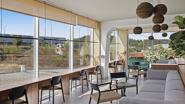 Een modern interieur met grote ramen, een zithoek met stoelen en een bank, en hangende, bolvormige lampen.