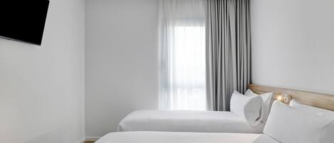 Habitación de hotel con dos camas, un televisor montado en la pared y una ventana con cortinas.