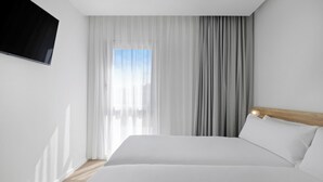 Hotelkamer met een groot bed, een flatscreen televisie aan de muur en een raam met dunne gordijnen.