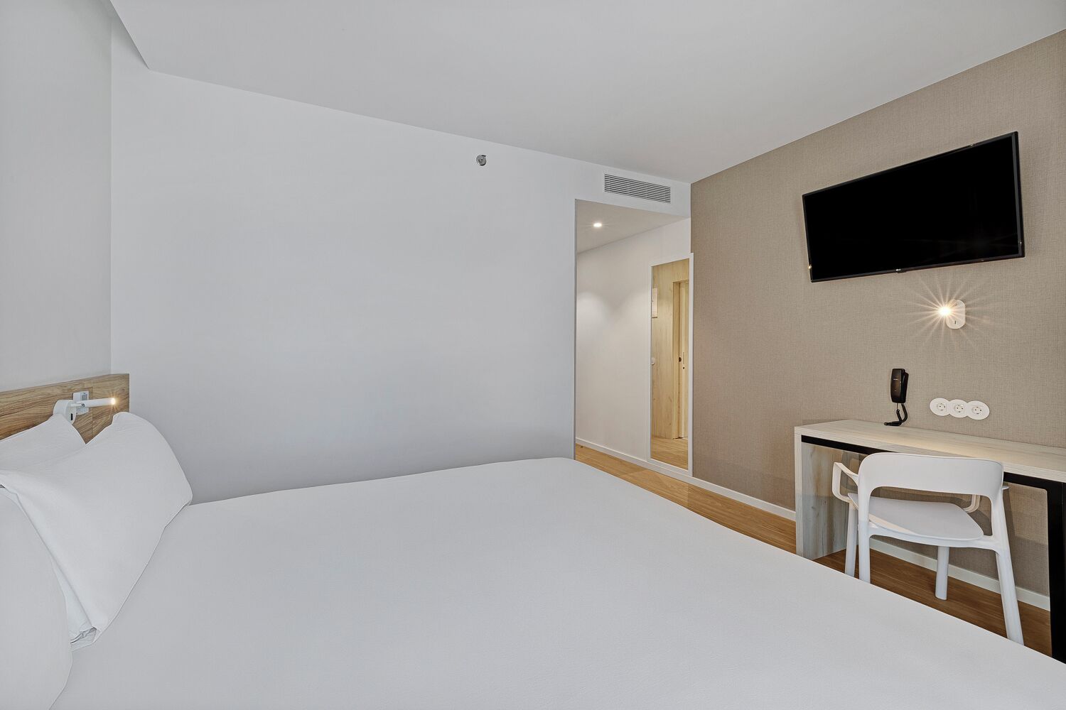 Habitación de hotel con cama, escritorio, silla, televisión de pantalla plana y teléfono en la pared.