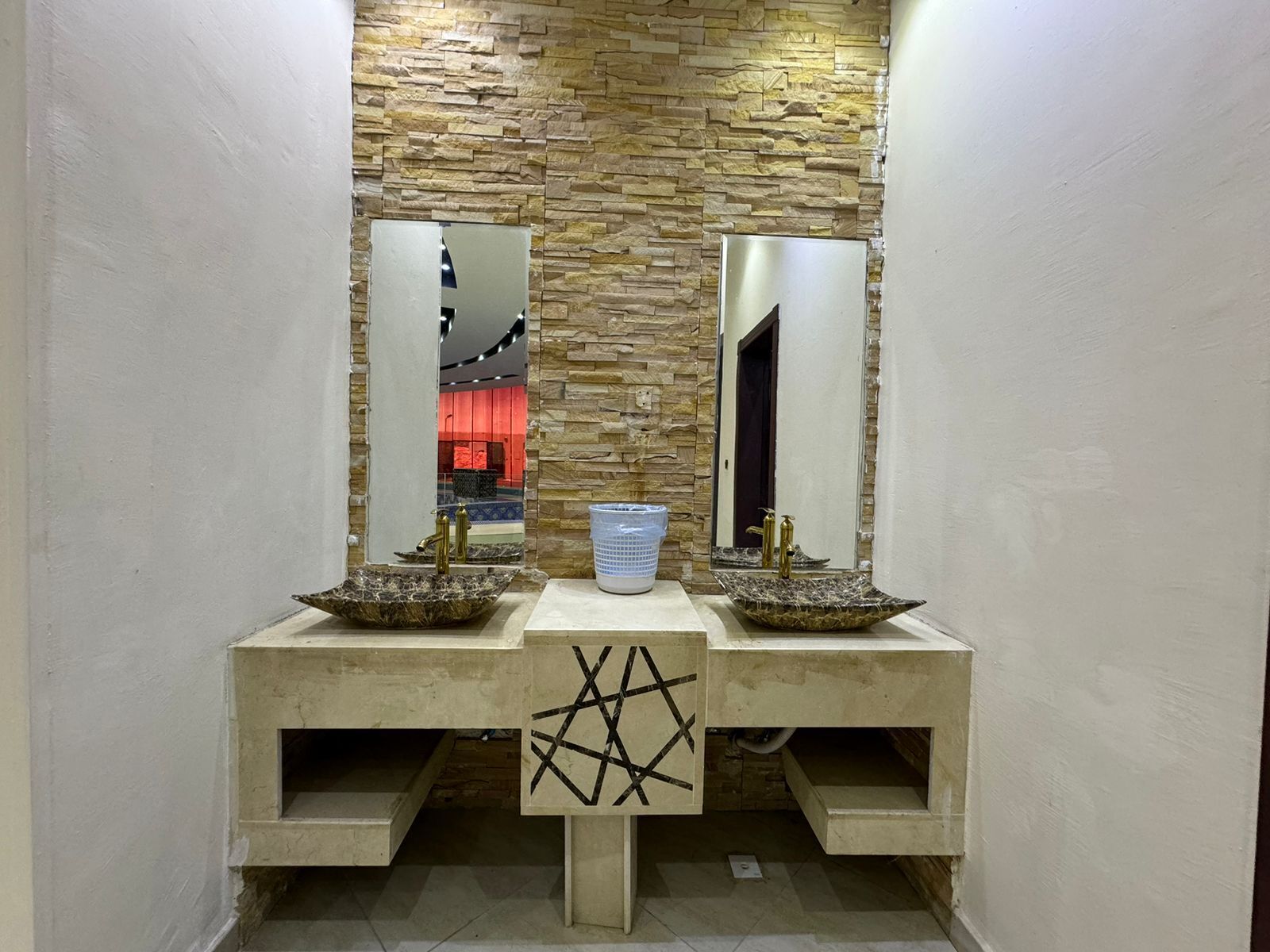 Une salle de bain dotée de deux lavabos, chacun avec un receveur en marbre et des robinets dorés, le tout mis en valeur par un mur en pierre à texture.