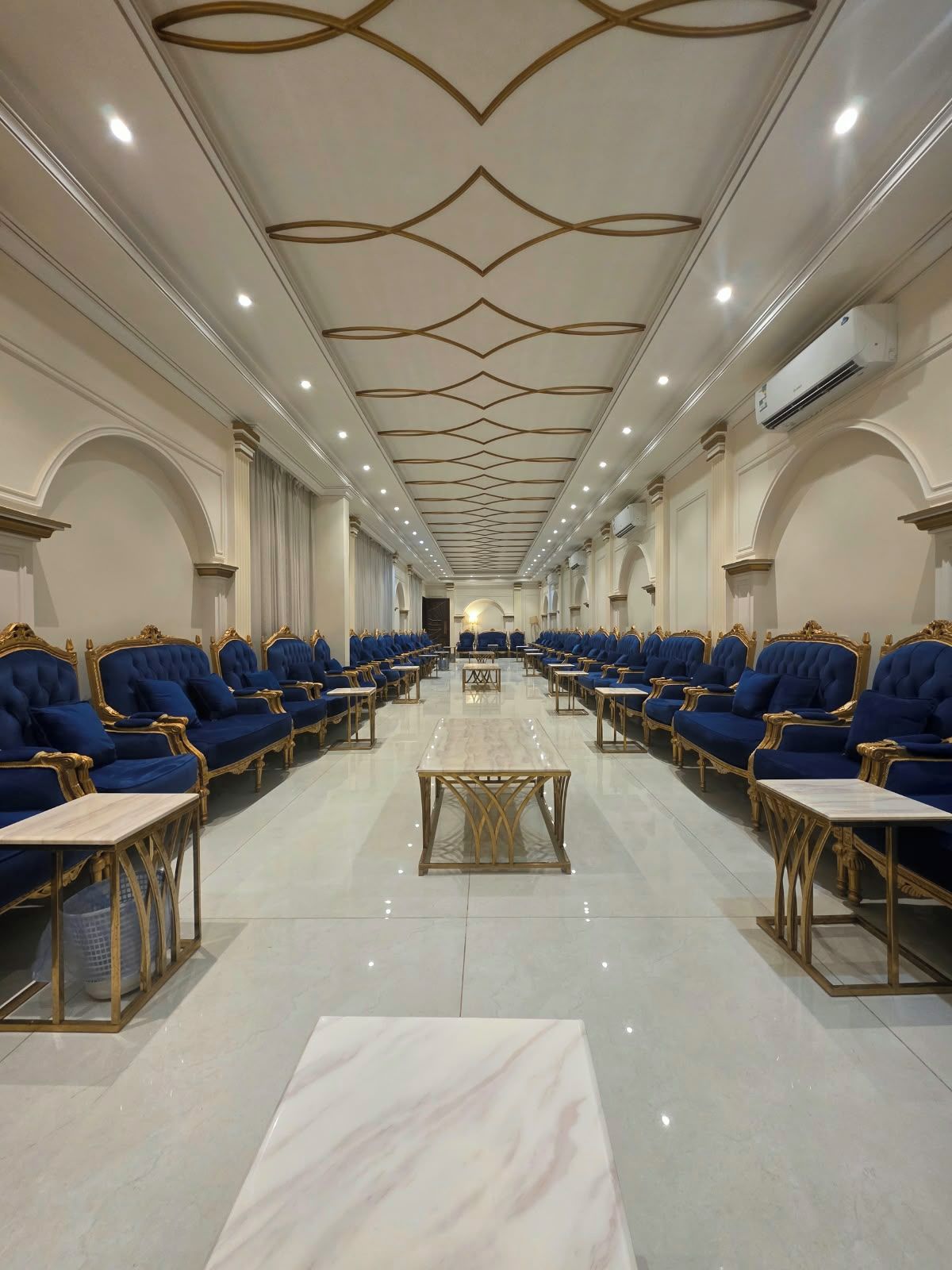 Un salón de conferencias de hotel con filas de sillas tapizadas en azul, una mesa central y un techo con diseños geométricos.