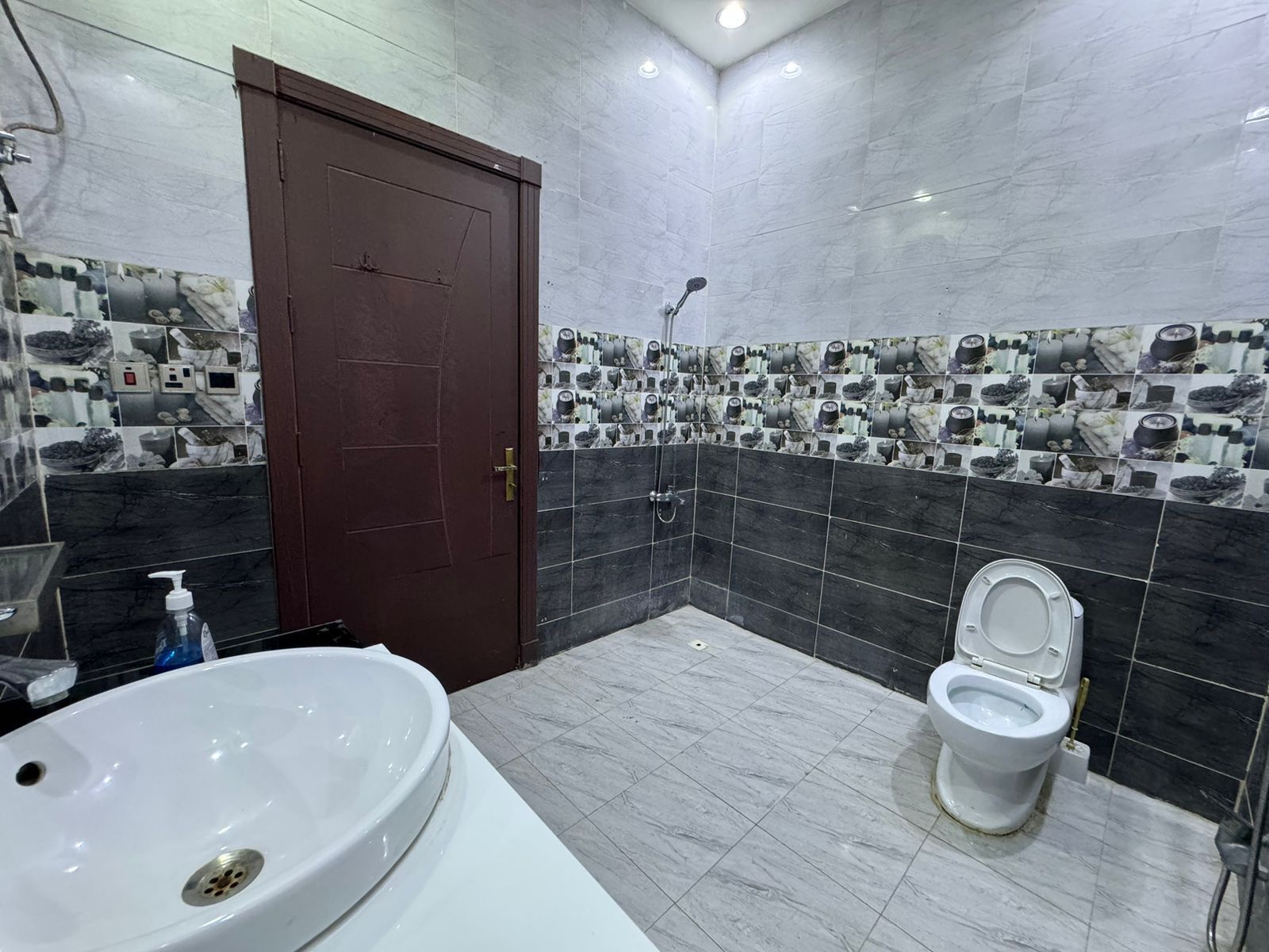 Un baño con lavamanos blanco, inodoro y ducha. Las paredes están cubiertas de azulejos con diseños en blanco y negro.