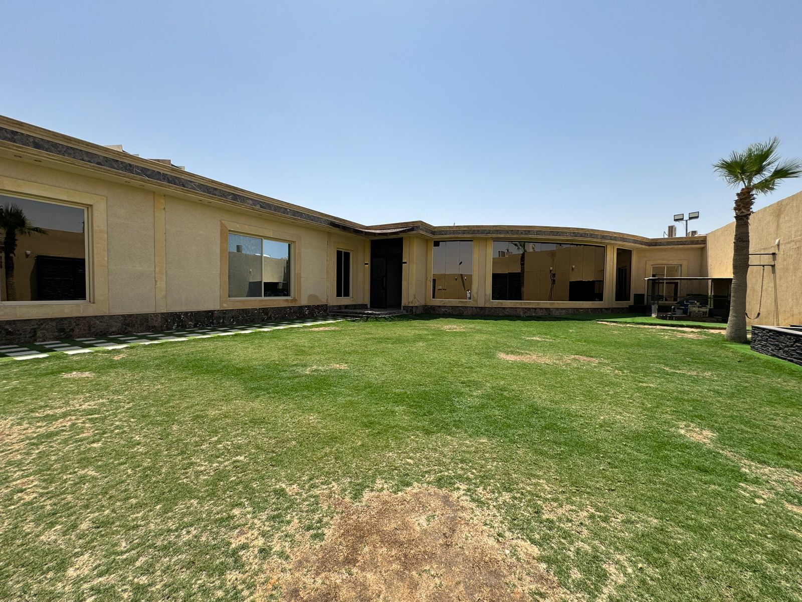 A modern house with a large lawn, a covered patio, and a pool area.