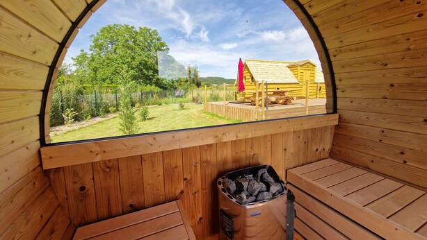 Una sauna de madera con techo curvo, un banco y un contenedor de basura.