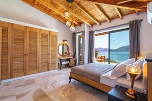 Quarto com teto de madeira, uma cama grande, escrivaninha com espelho e vista para o mar.