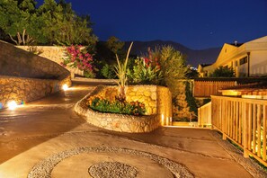 A stone pathway leading to a stone planter with flowers and a wooden fence.