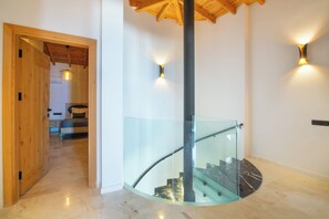 A modern interior with a glass staircase, wooden door, and a ceiling with exposed beams.