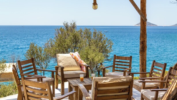 A wooden outdoor seating area with a view of the sea and a distant island.