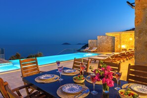 A dining table set for two with a view of the sea and a pool.