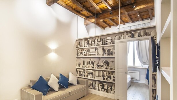 A modern room with a wooden ceiling, a sofa with blue and white cushions, and a wall of shelves filled with various items. - Ciambella Atmosphere apartment (Rome)