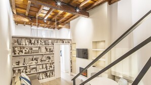 A modern interior with exposed wooden beams, a staircase with glass railings, and a collection of decorative items on shelves. - Ciambella Atmosphere apartment (Rome)