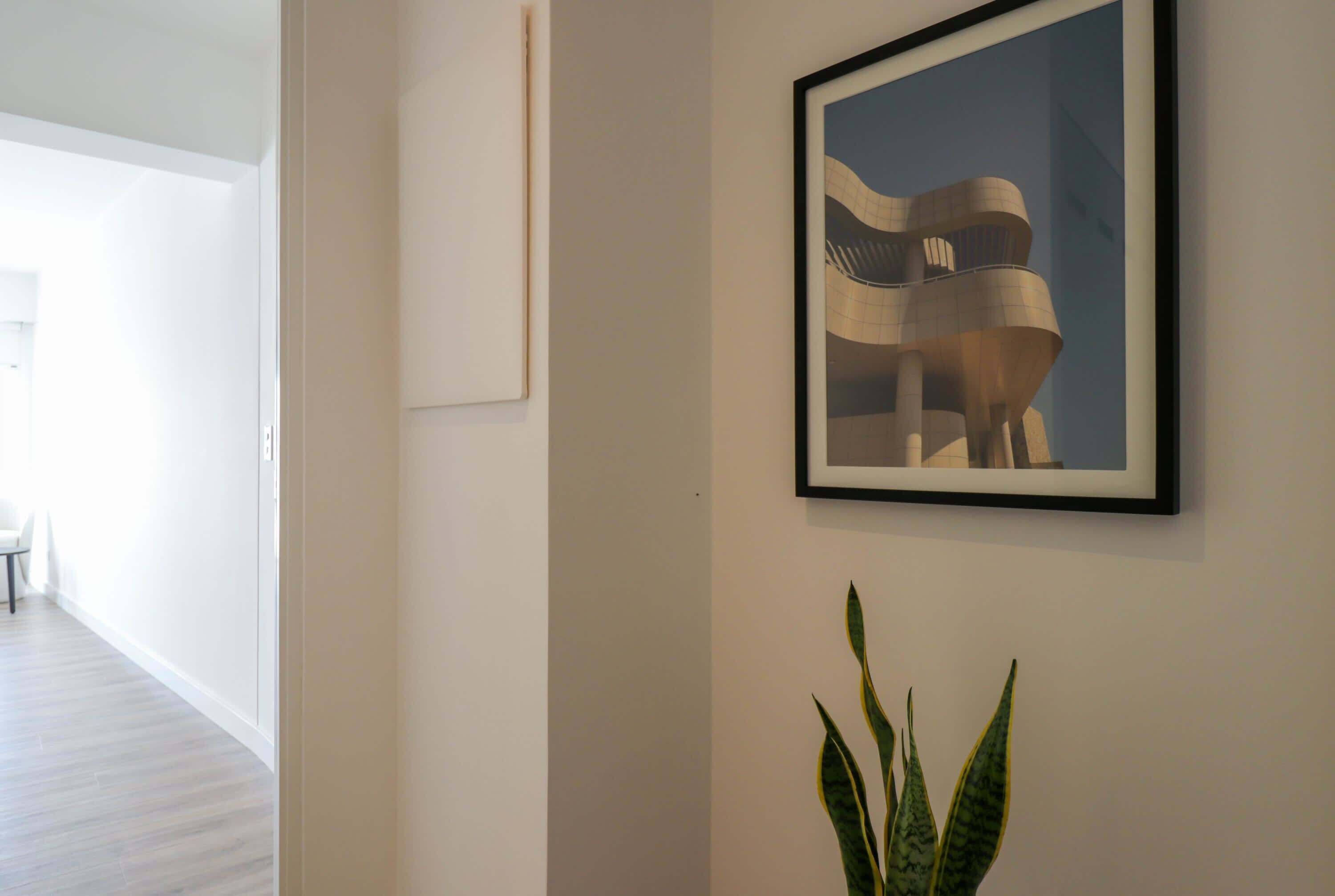 Ein Flur mit einem gerahmten Architekturprint an der Wand, einer Kübelpflanze und einem Blick auf einen Essbereich im Hintergrund.
