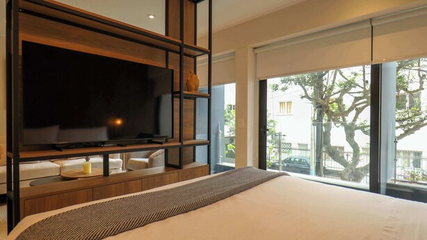 Ein modernes Hotelzimmer mit einem großen Bett, einem Flachbildfernseher an einer Holzablage, einer Couch und einem großen Fenster mit Blick ins Freie.