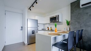 A modern kitchen with a stainless steel refrigerator, a microwave, and a water dispenser. There is a small island with bar stools and a potted plant. - w* | Minimalist 1BR w/ Balcony in San Francisco (Panamá)