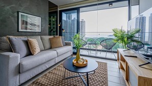A modern living room with a grey sofa, a round coffee table with decorative items, and a view of high-rise buildings through large windows. - w* | Minimalist 1BR w/ Balcony in San Francisco (Panamá)