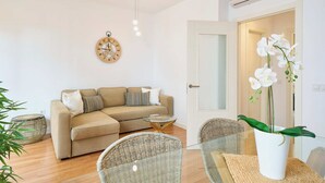 Ein Wohnzimmer mit einem beigefarbenen Sofa, Korbstühlen und einem runden Couchtisch, dazu eine Orchidee im Topf.