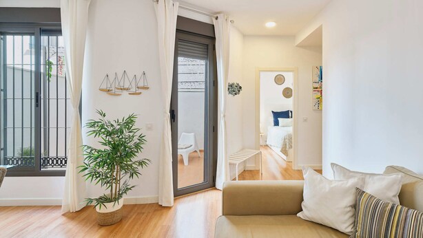 Ein modernes Wohnzimmer mit einer Couch, einem Topfpflanzen und einer Glastür zum Balkon.