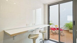 Eine moderne Küche mit weißer Arbeitsplatte, zwei Barhocker und einer Schiebeglastür, die auf eine Außenpatio mit Tisch und Stühlen führt.