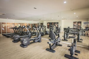 A gym with various cardio machines, weightlifting equipment, and a large mirror wall.