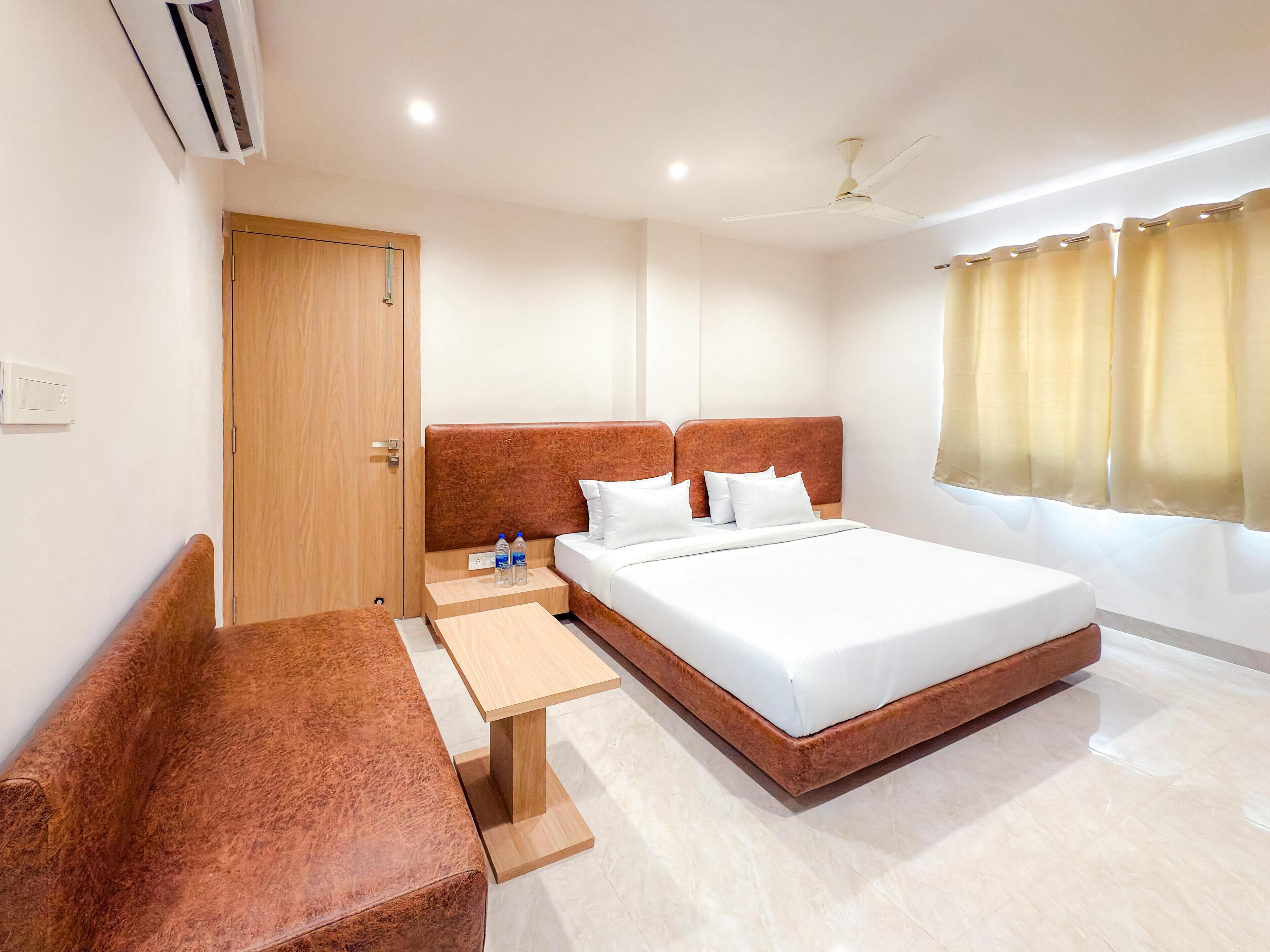 A hotel room with a large bed, a wooden bench, a small table, and a ceiling fan.
