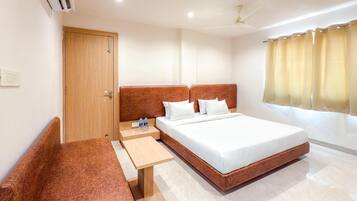 A hotel room with a large bed, a wooden bench, a small table, and a ceiling fan.