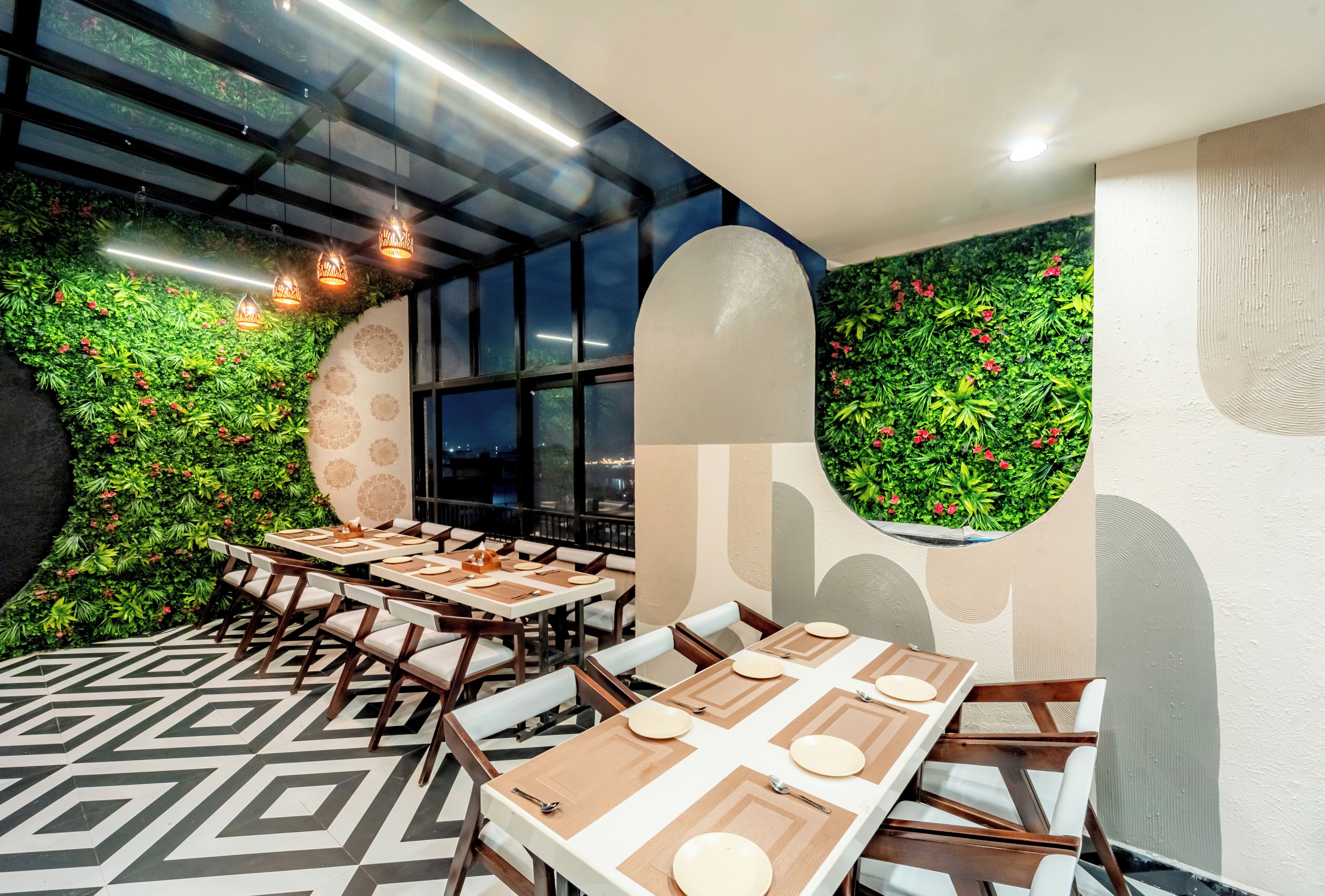 A restaurant with tables set for dining, surrounded by green foliage and decorative wall elements.