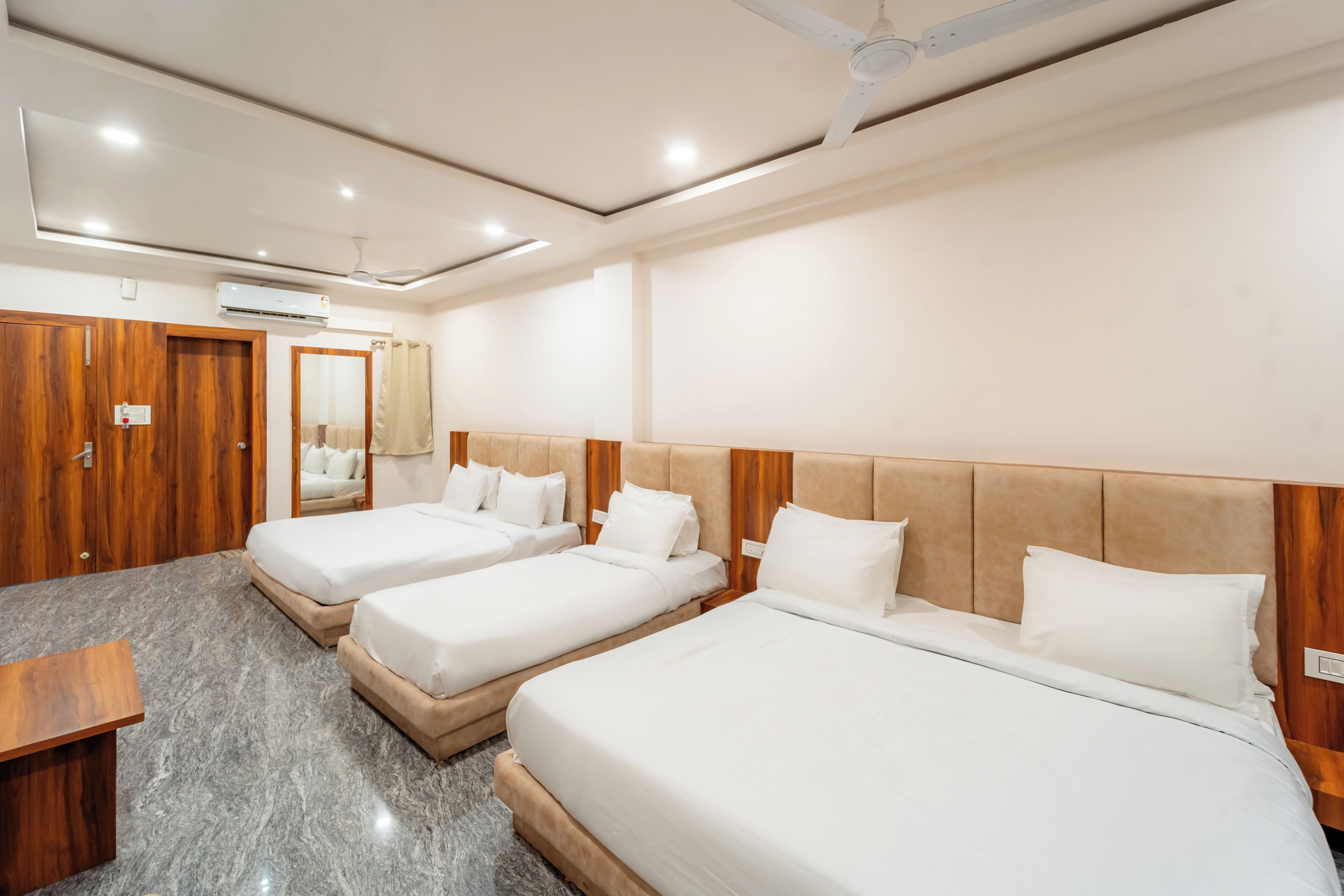 A hotel room with three beds, wooden wardrobe, and a mirror.