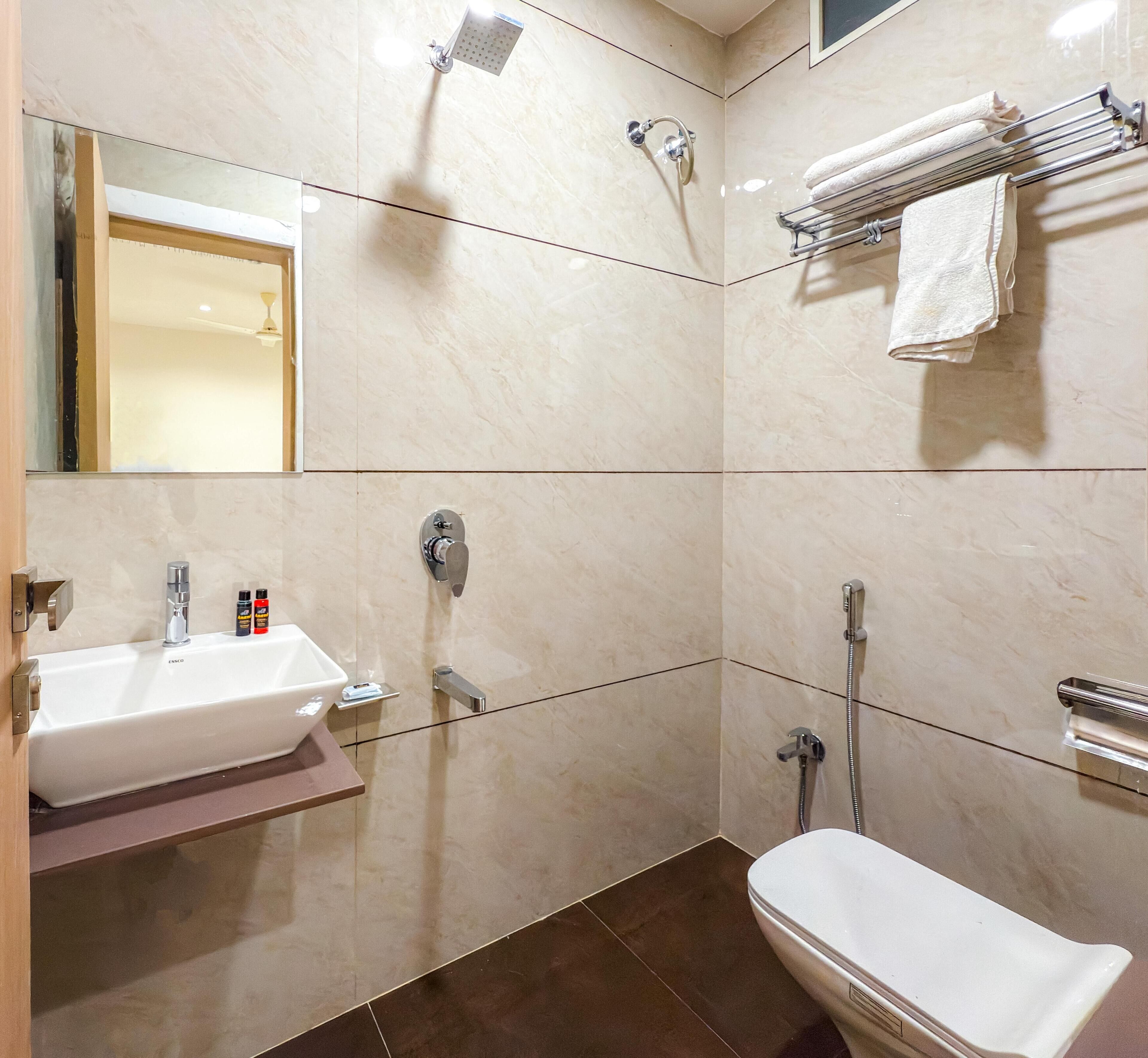 A modern bathroom with a white sink, mirror, and toilet. There is a shower with a handheld showerhead and a towel rack with folded towels.