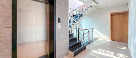 A modern elevator with a marble wall, a staircase with metal railings, and a wooden door.