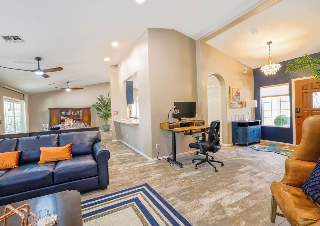 A spacious living area with a dark blue sofa, a wooden coffee table, and a desk with a computer.