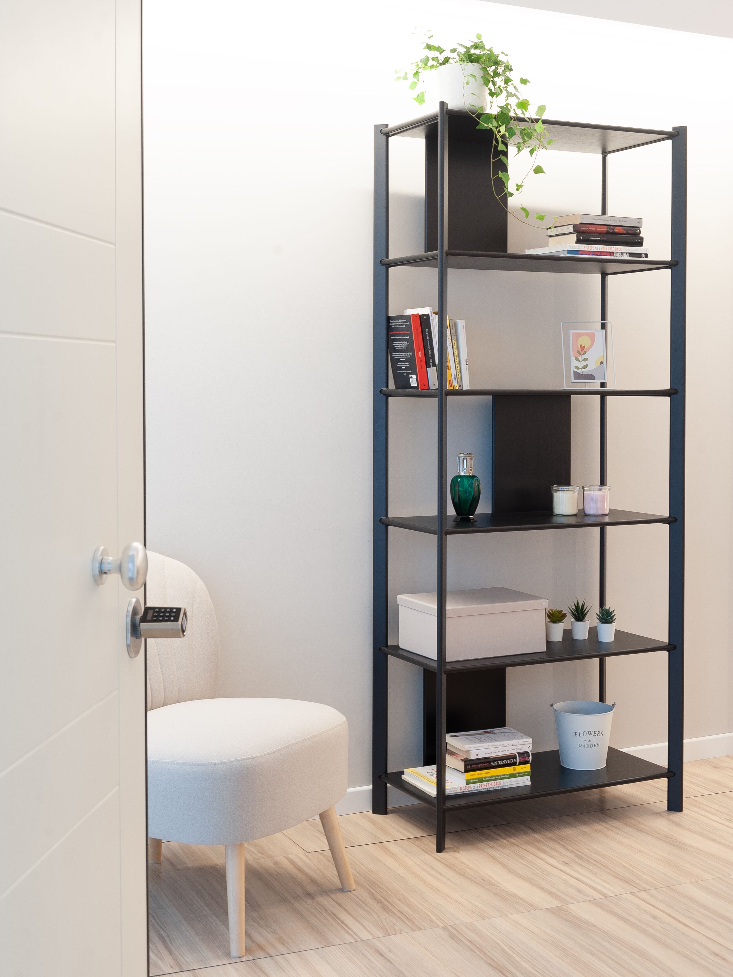 Une pièce moderne avec une porte blanche, une chaise grise, une bibliothèque noire et une petite plante en pot.