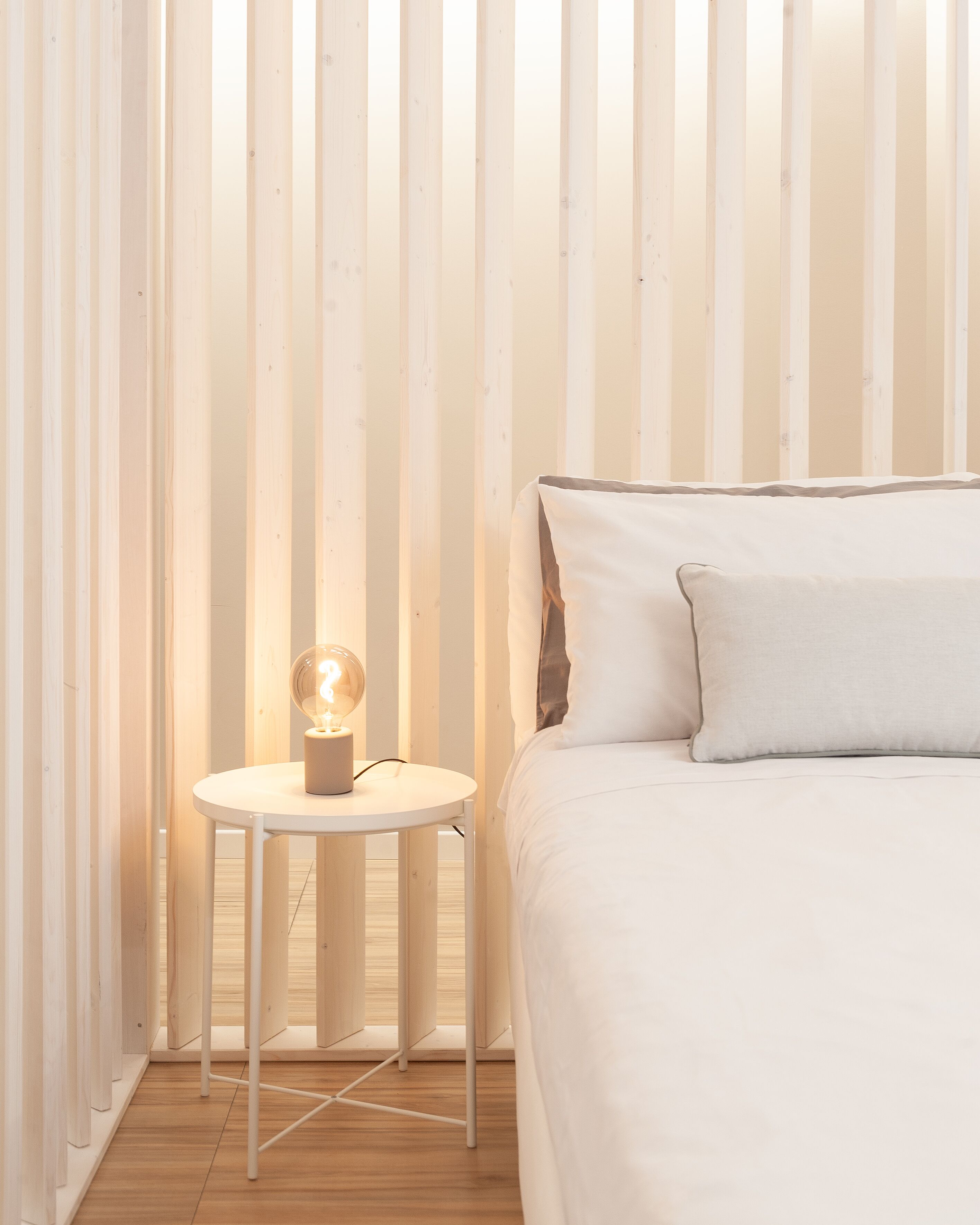 A bedroom with a bed, a bedside table with a lamp, and wooden slats on the wall.