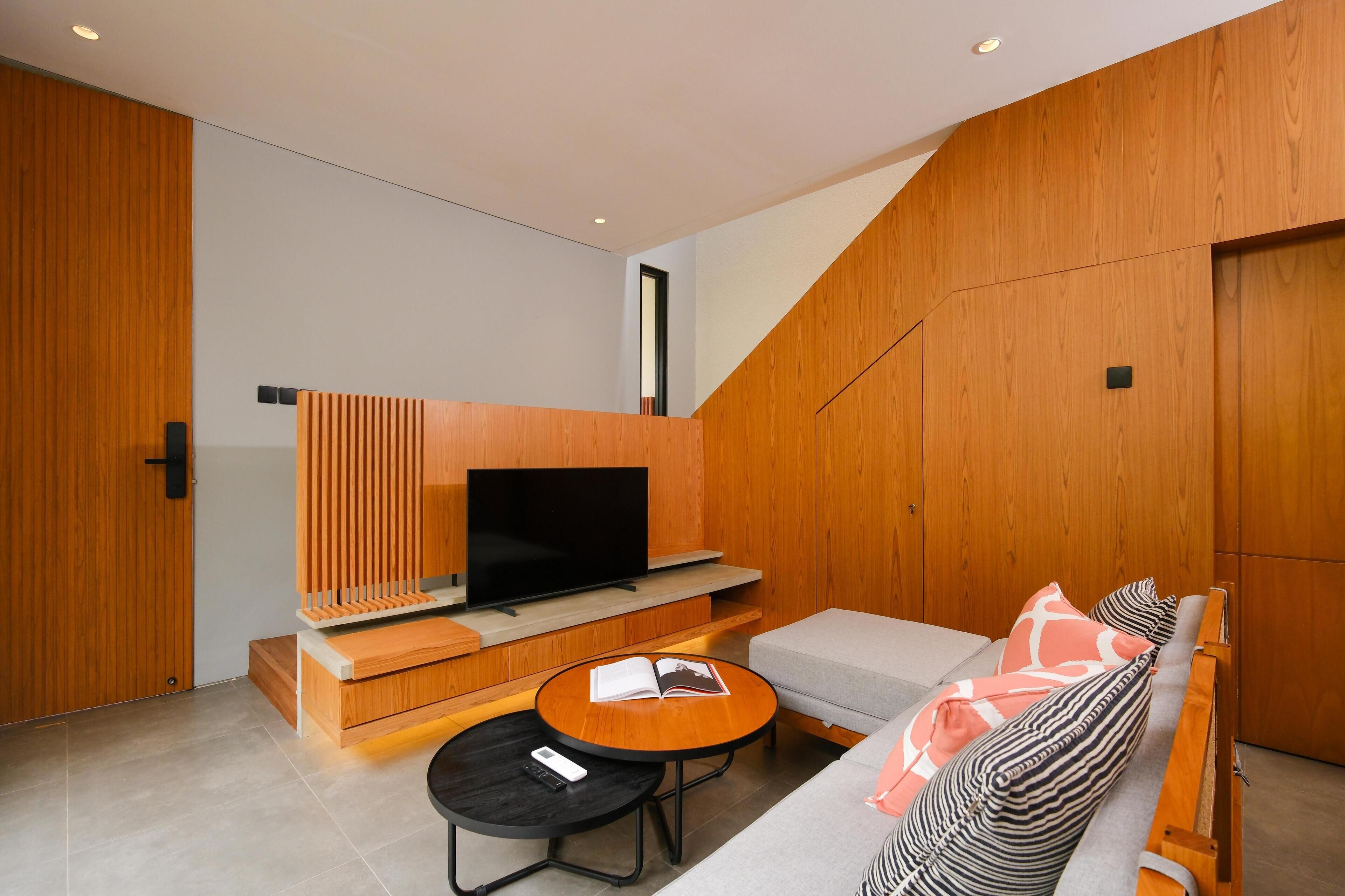 Un soggiorno moderno con una TV a schermo piatto, pareti rivestite in legno, un divano, un tavolino da caffè e un piccolo tavolino laterale.