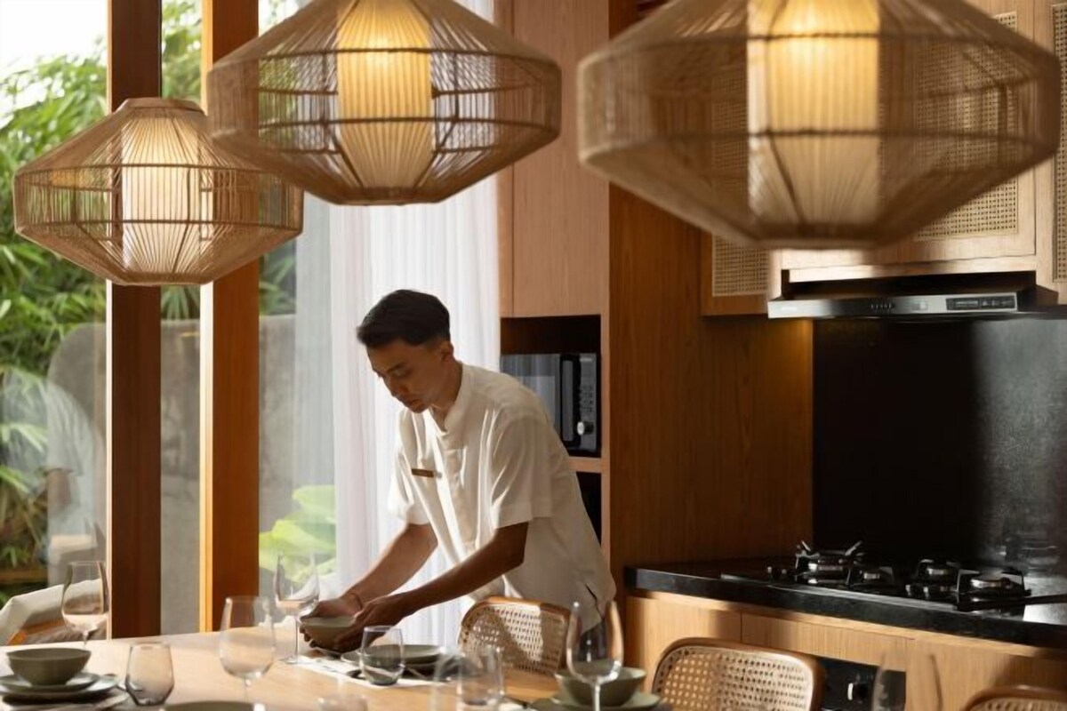 A chef preparing food in a modern kitchen with a dining area visible through large windows.