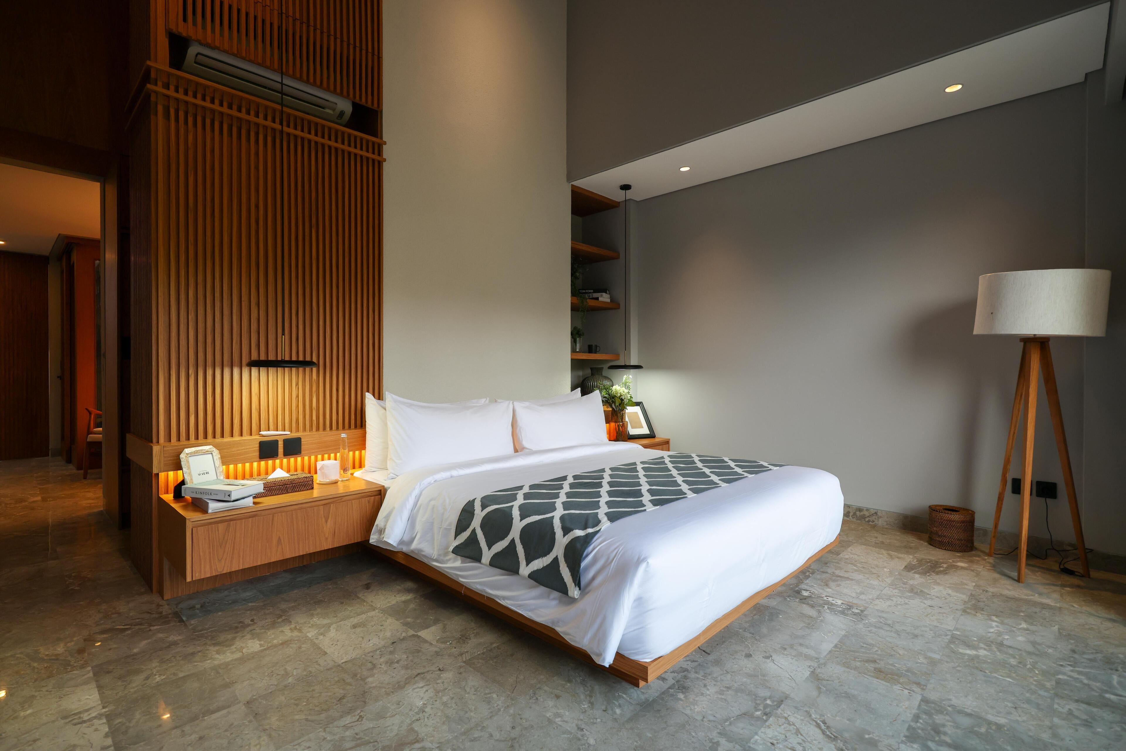 Quarto de hotel moderno com uma cama grande, painéis de madeira, uma mesa com telefone e um abajur.