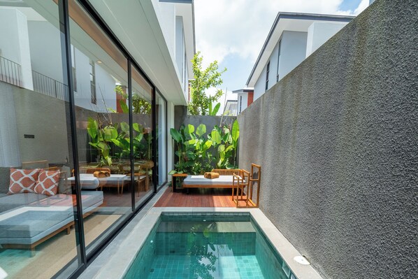 A modern outdoor pool area with a glass-enclosed seating area, a wooden deck, and lush greenery. - Alaya Private Estate at Damara Village Ubud (Ubud)