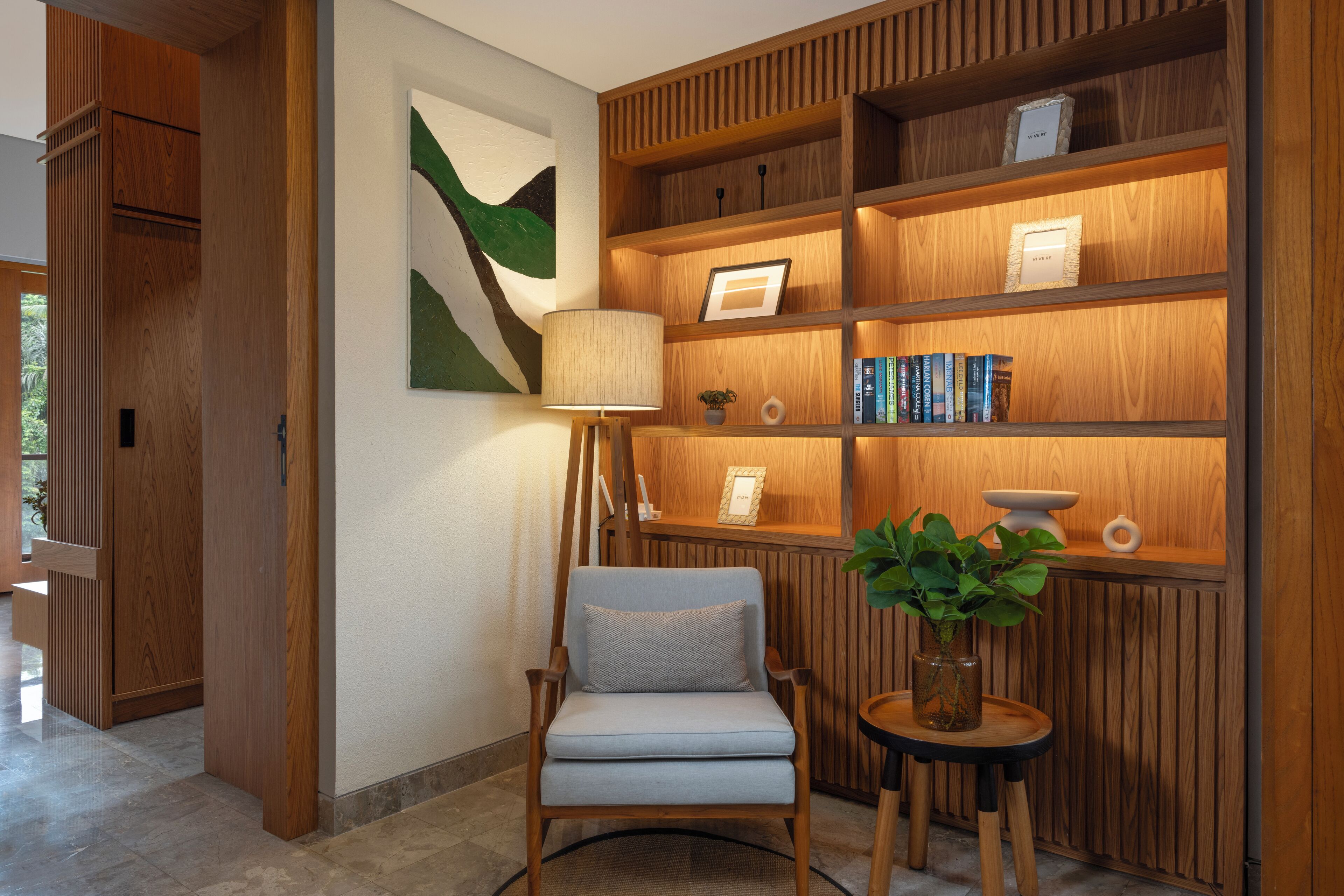 A modern interior with a wooden bookshelf, a comfortable armchair, and a small table with a plant.