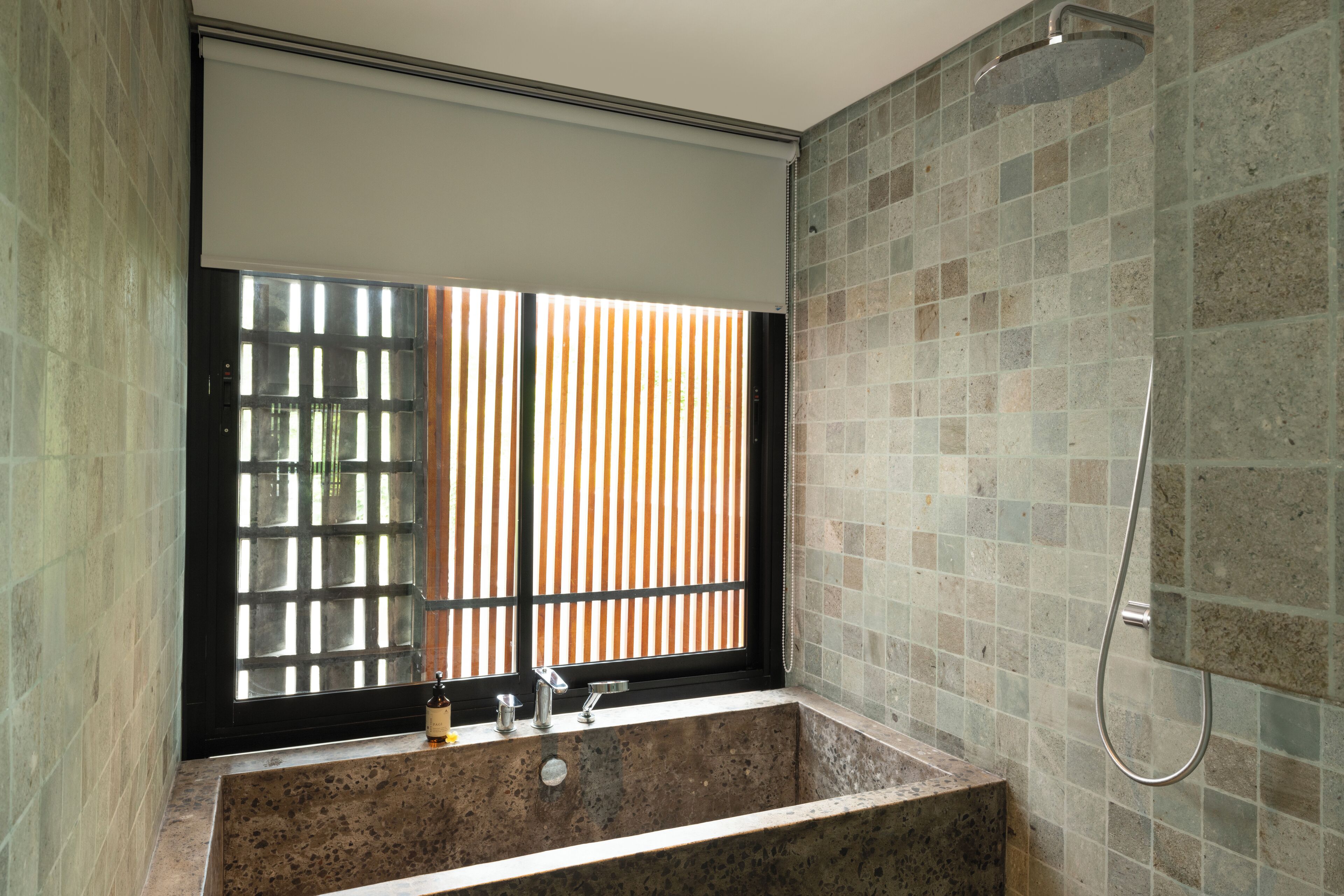 A bathroom with a bathtub, a window with blinds, and a shower area.